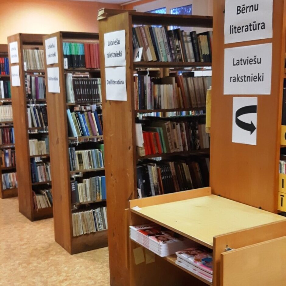 Aizputes vidusskolas bibliotēkas telpa ar grāmatu plauktiem.